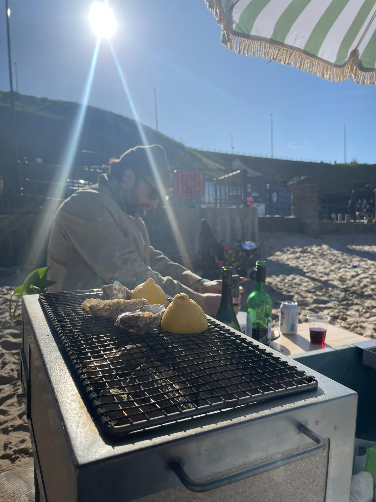 Grilling oysters on the beach with a striped umbrella overhead