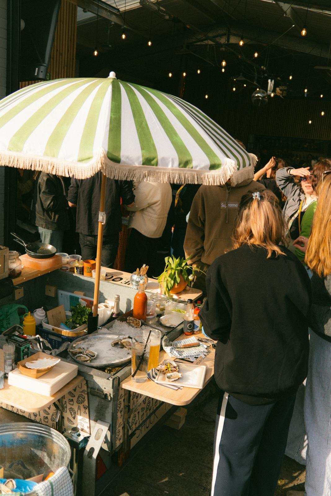 The O Co. trailer at a busy event under a striped umbrella